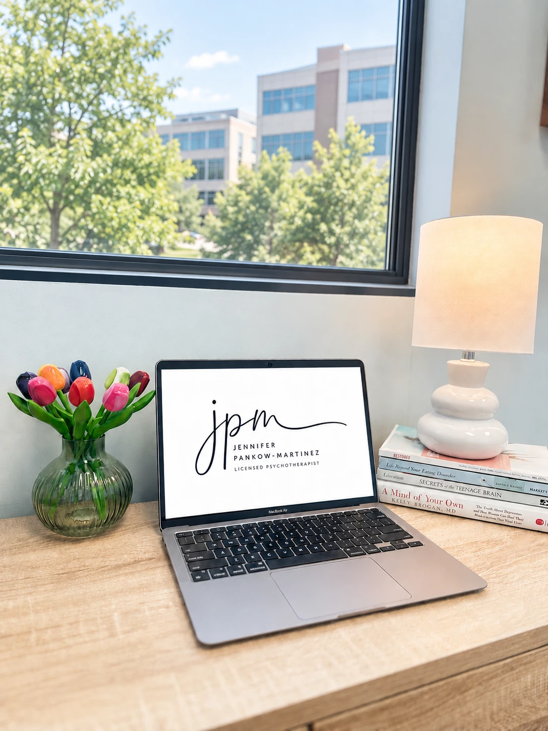 Jennifer's office desk with the JPM logo displayed on a laptop beside colorful tulips and a lamp