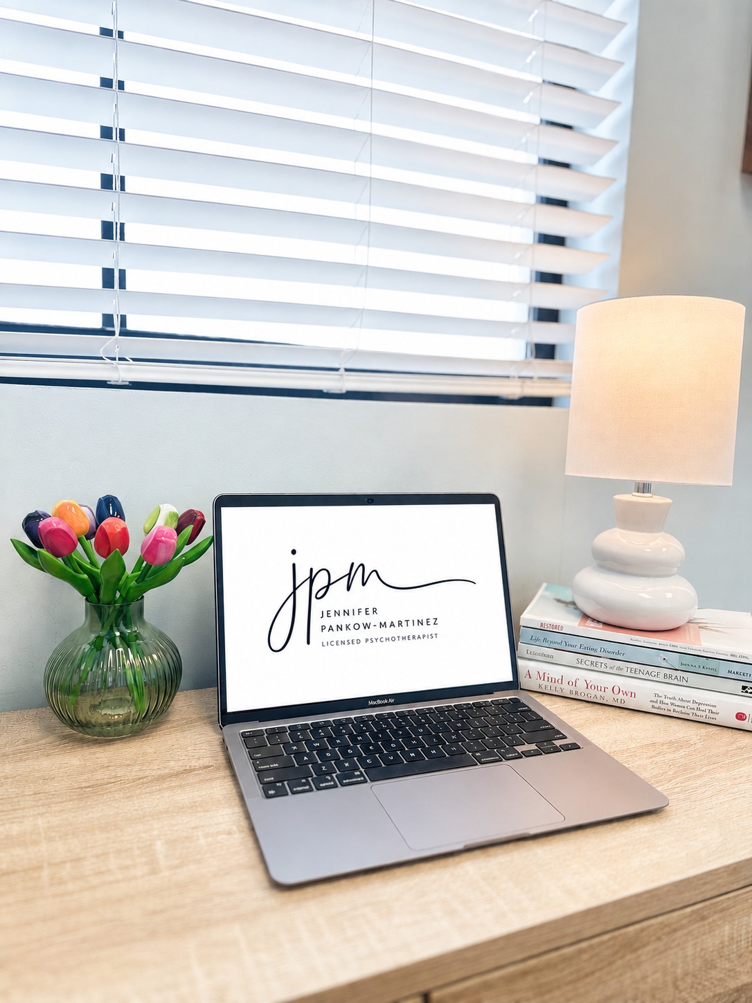 Jennifer's office desk with the JPM logo displayed on a laptop beside colorful tulips and a lamp