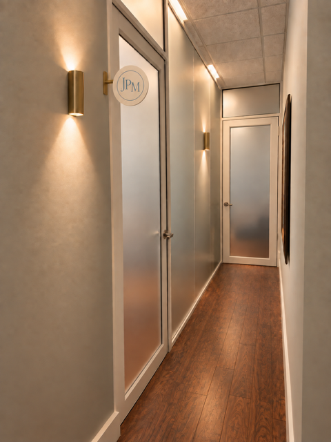 Hallway at Jennifer’s office, with warm wall lighting and a round JPM sign beside the door